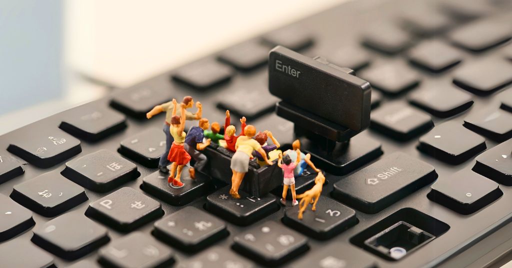 Miniature art figures appear to push the Enter key on a keyboard.